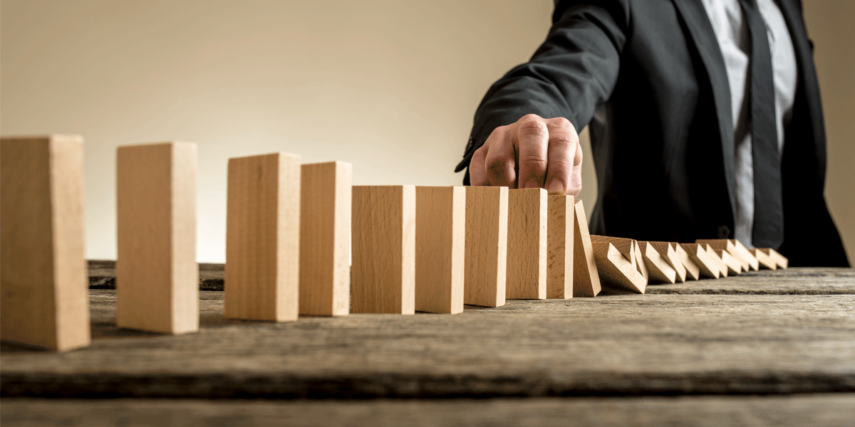 Man pushing over a stack of blocks; the concept of a domino effect.